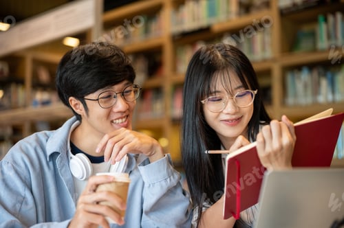 Preview: Glasses asian woman student writing in book holding over laptop with man friend at table in library.