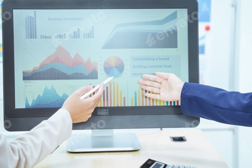Preview: Two young Asian businesswomen sit at a table, engaged in a meeting.examine graphs and discuss