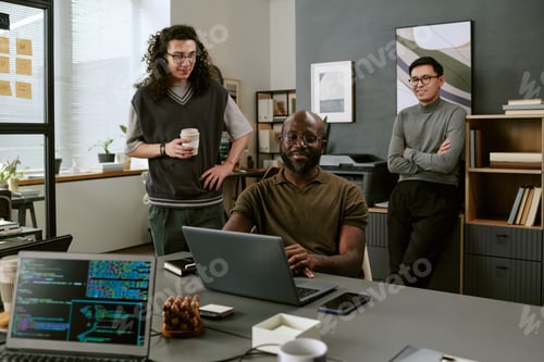 Preview: Young Black Man Smiling While Working on Laptop with Diverse Coworkers