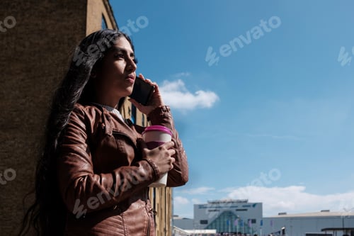 Preview: Young indian woman with long hair using phone outdoors.
