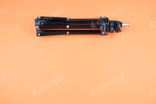 Preview: Closeup shot of a black iron folding tripod on orange background with a copy space