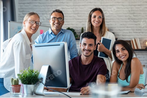 Preview: Successful business team standing around computer while looking at camera in the coworking space