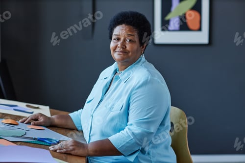 Preview: Confident mature African American craftswoman sitting by workplace in studio