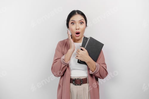 Preview: A shocked young Asian student wearing cardigan while holding books with her mouth wide open.