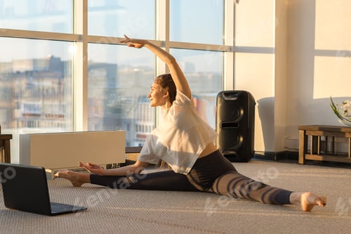 Preview: woman practicing yoga,Splits exercise in front of a laptop.Yoga and fitness online training concept