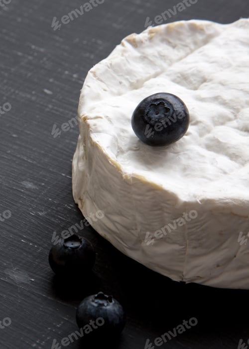 Preview: Camembert cheese with blueberries on a black background, side view. Food for wine. Close-up.