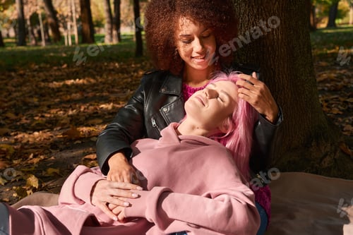 Preview: Romantic lesbian couple resting in park on sunny autumn day