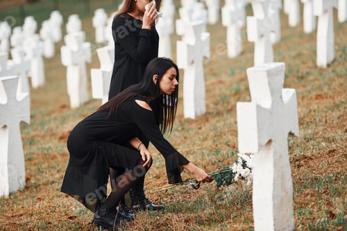 Preview: Two young women in black clothes visiting cemetery with many white crosses