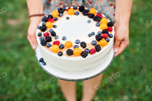 Preview: Midsection of woman holding birthday cake outdoors in garden in summer.