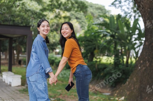 Preview: Two smiling young women holding hands and turning around in a park