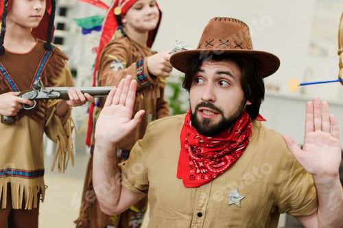 Preview: father in hat and bandana and little sons in indigenous costumes with toys playing together at home