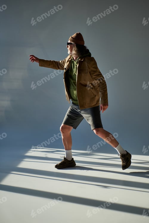 Preview: full length of senior man in fashionable casual clothes, dark sunglasses, beanie hat, jacket