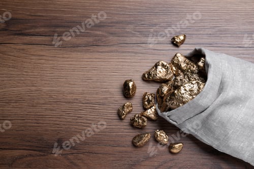 Preview: Overturned sack of gold nuggets on wooden table, flat lay. Space for text
