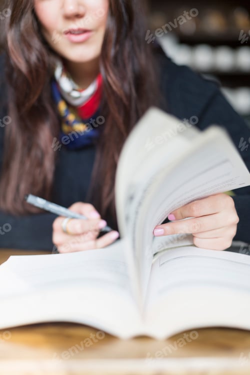 Preview: Midsection of woman turning pages of book in cafe