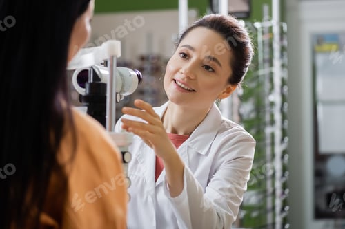 Preview: positive ophthalmologist pointing with hand near blurred woman and vision screener
