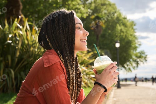 Preview: Young latina woman with braids enjoying a refreshing drink in the park