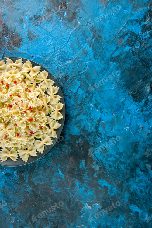 Preview: Half shot of raw Italian farfarelle pasta with vegetables on blue background in overhead view