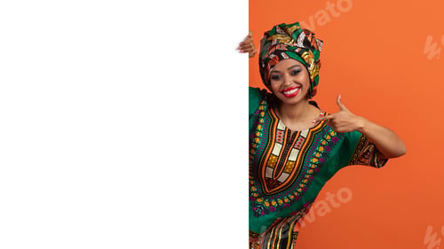 Preview: Cheerful african woman in traditional costume pointing at advertising board