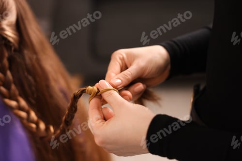 Preview: Hairstylist braiding girl's hair in salon, closeup