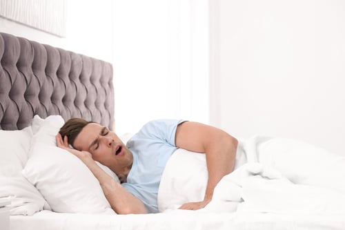 Preview: Young man yawning in bed with pillows at home