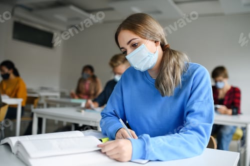 Preview: Young students with face masks at desks at college or university, coronavirus concept.