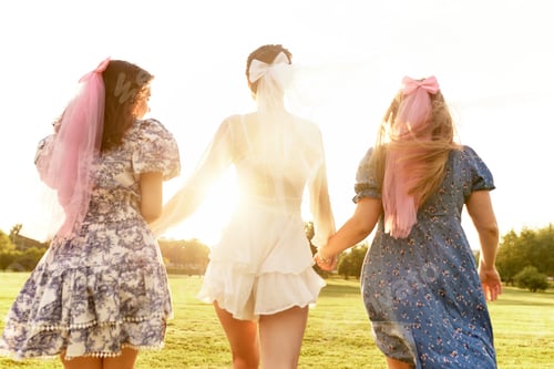 Preview: Happy charming bride in a white dress with a white veil and two bridesmaids with pink veils walking