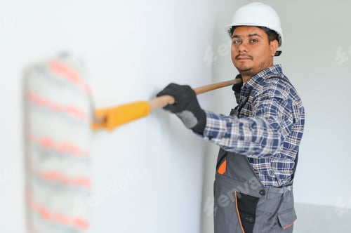 Preview: An Indian apartment repair worker paints a white wall with a roller.