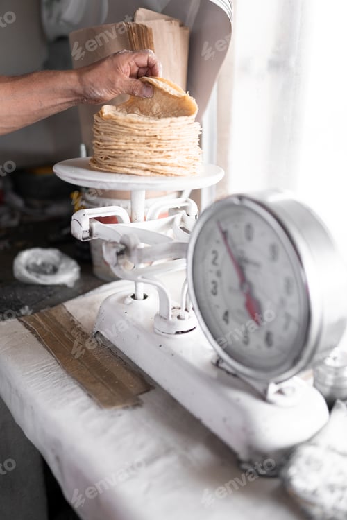 Preview: An adult tortilla maker is weighing a stack of tortillas using an analog scale