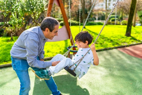 Preview: Grandfather pushing grandson on swing at the playground
