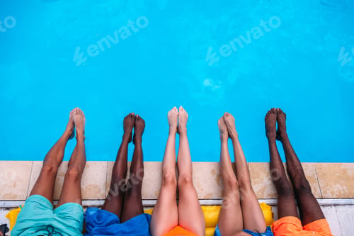 Preview: Young people lying near swimming pool. Cropped image of legs over blue water