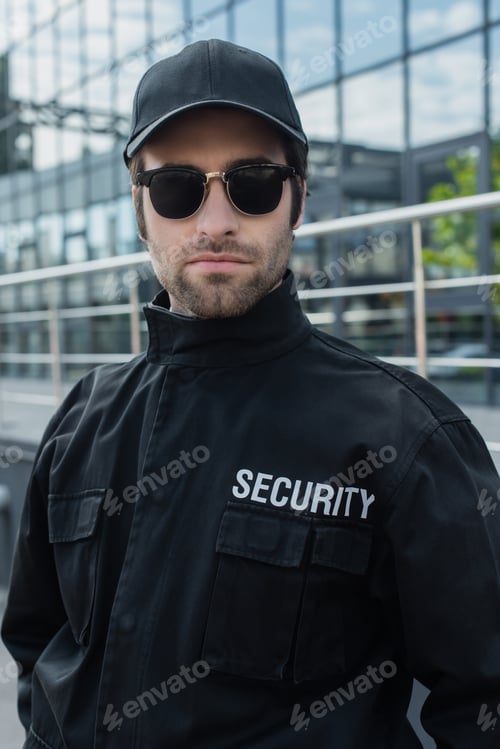 Preview: security man in black uniform and sunglasses looking at camera outdoors