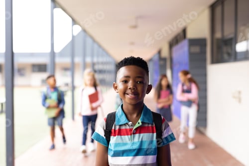 Preview: Vertical portrait of smiling african american boy in elementary school corridor, with copy space