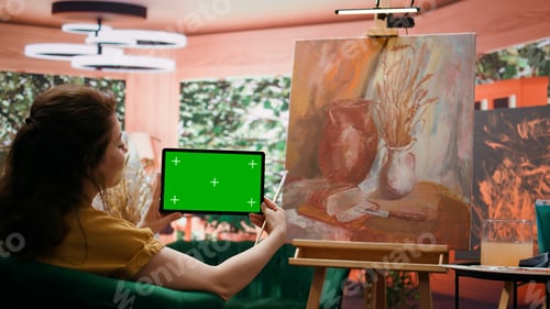 Preview: Painter holding a device with isolated mockup screen in her art studio