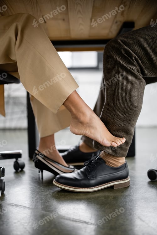 Preview: cropped view of young african american woman seducing businessman under office desk
