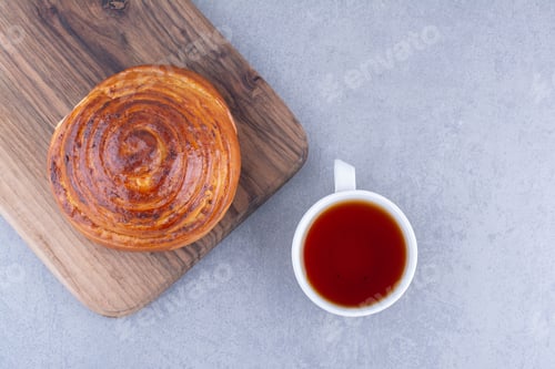 Preview: Sweet bun on a board next to a cup of tea on marble background