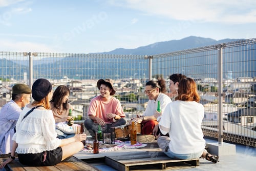 Preview: Group of young Japanese men and women sitting on a rooftop in an urban setting, drinking beer.