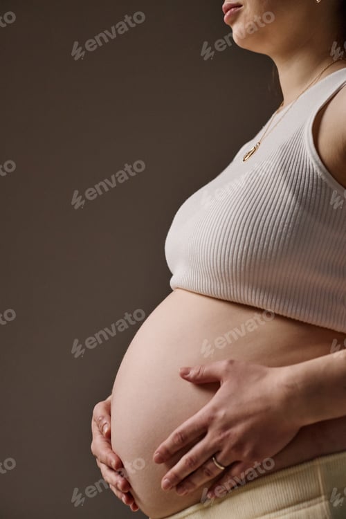 Preview: Vertical of Caucasian Young Adult Woman Holding Pregnant Belly in Studio