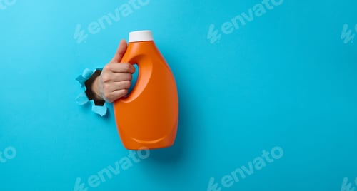 Preview: Orange plastic bottle with liquid detergent in a female hand on a pink background
