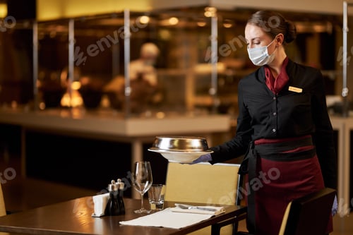 Preview: Serious young woman in mask working at restaurant