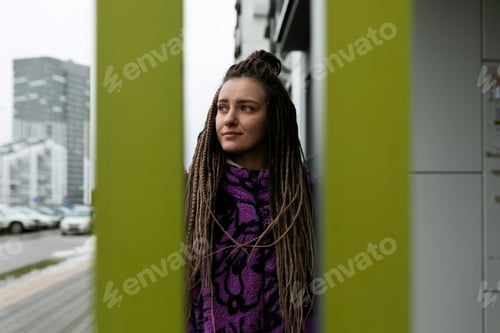 Preview: Lifestyle concept. A young pretty woman with dreadlocks and piercings stands at the entrance to a