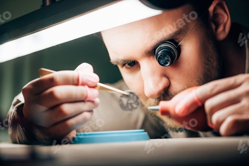 Preview: Selective focus of watchmaker working with watchpart and blower by lamp on table