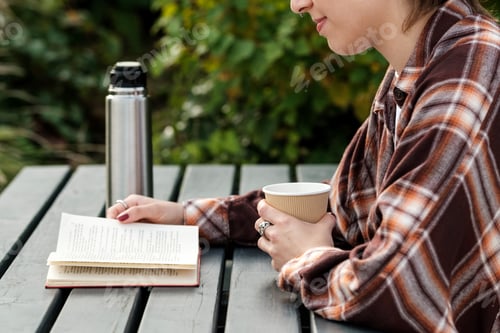 Preview: Student reading a book and drinking coffee outdoors in autumn