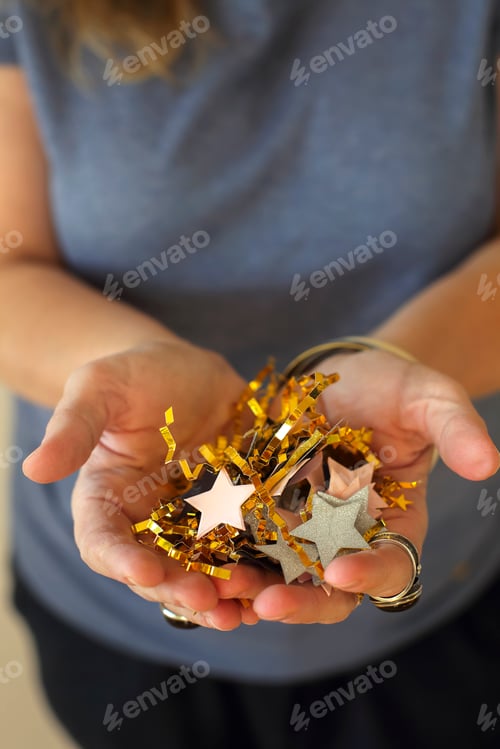 Preview: Middle-aged woman holding gold and silver star shapped birthday confetti in hands