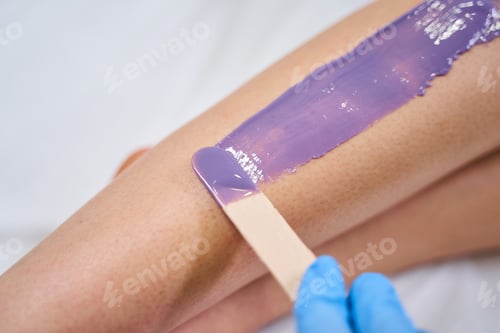 Preview: Professional beautician putting wax on female leg