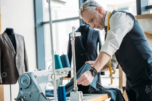 Preview: handsome tailor looking at cloth at sewing workshop