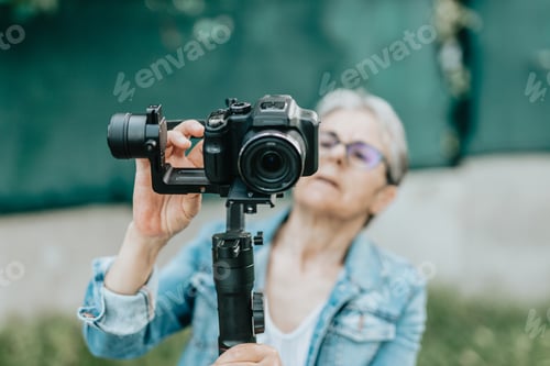 Preview: Concentrated senior woman arranging and preparing to record with her camera, photos and videos.