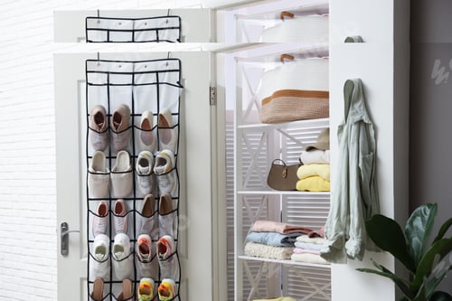 Preview: Organizer with different footwear on door and clothes indoors. Shoe storage