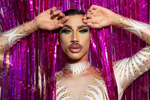 Preview: portrait of beautiful young man in drag queen makeup looking at camera and colorful background