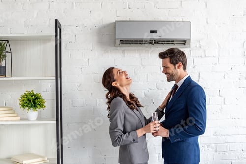 Preview: cheerful businesspeople laughing while standing under air conditioner in office