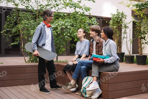 Preview: Group of young cool students sitting on bench and speaking while spending time together